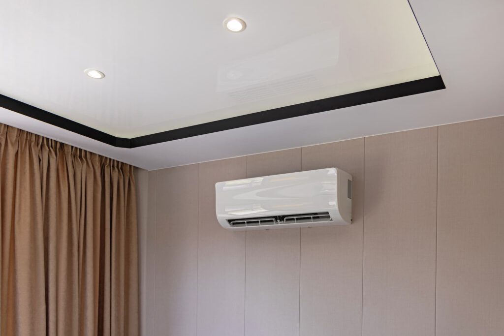 Wall-mounted split air conditioning system installed in a modern room with recessed ceiling lighting and curtains.