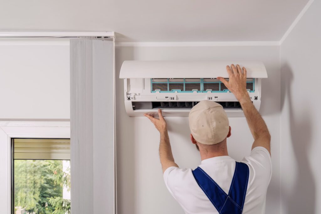 Technician opening a wall-mounted air conditioning unit for servicing and maintenance.