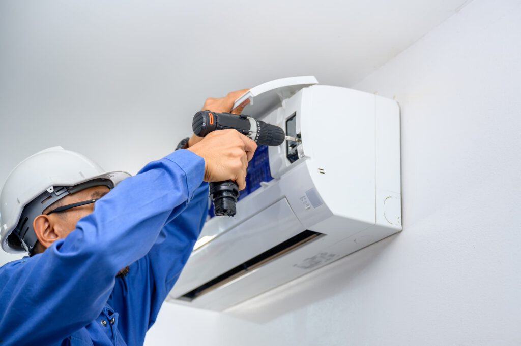 HVAC technician installing a wall-mounted split system air conditioning unit with a power drill.