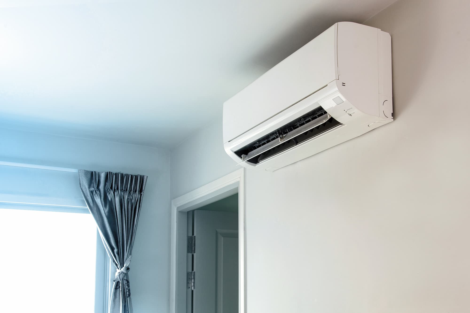 Wall-mounted split system air conditioner installed in a modern bedroom near a window and doorway.
